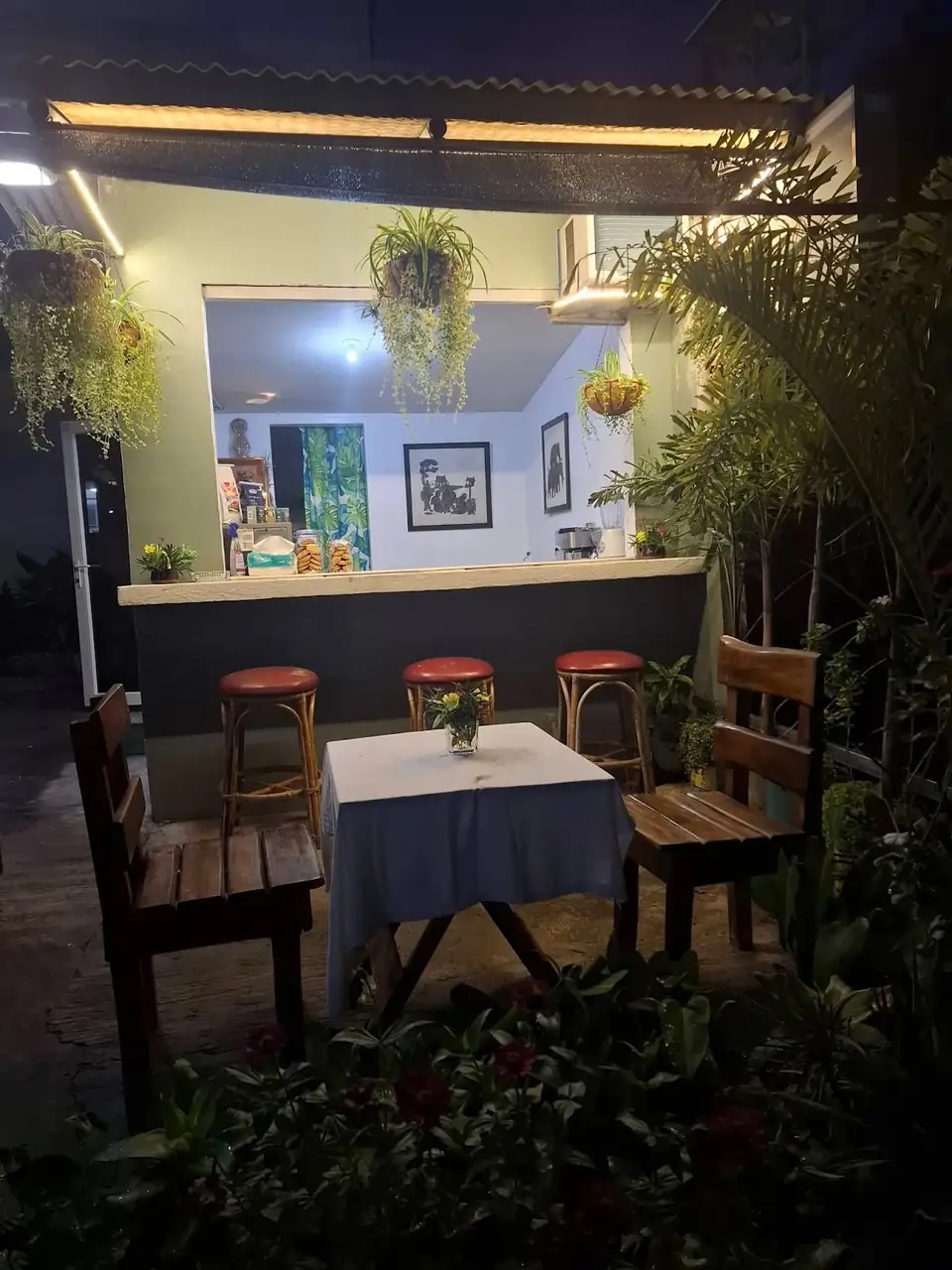 Ang bukas na counter at mga kahoy na upuan sa hardin ng Kape Parola na may ilaw sa gabi