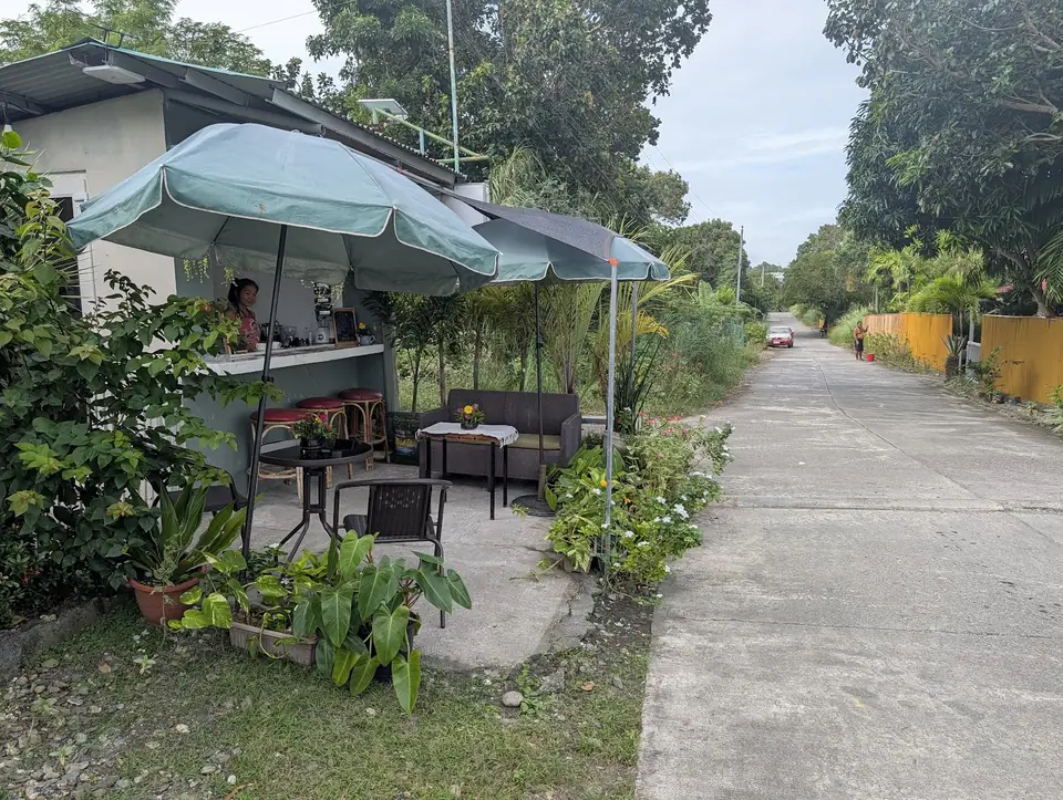 Ang bukas na roadside counter at mga upuan ng Kape Parola sa tabi ng sementadong daan papunta sa parola