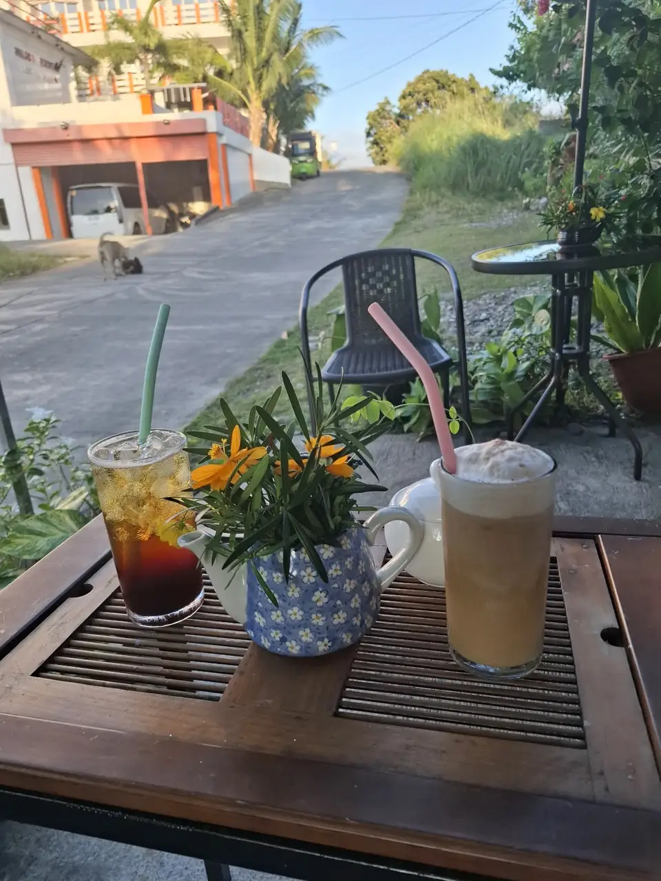 Isang malamig na maitim na inumin at mataas na mabula na kape sa kahoy na mesa na may kulay-kahel na mga bulaklak